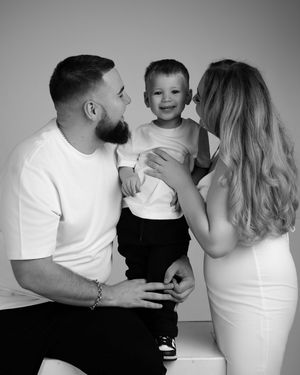 Black and white portrait of a family of three sharing an intimate moment together against a simple backdrop.