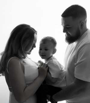 Black and white intimate family portrait showing tender moment between parents and young child in soft lighting.
