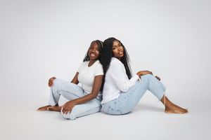 A person wearing light blue jeans and a white top poses gracefully on a white studio floor.