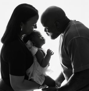 A silhouetted family of three shares an intimate moment together in black and white against a bright background.