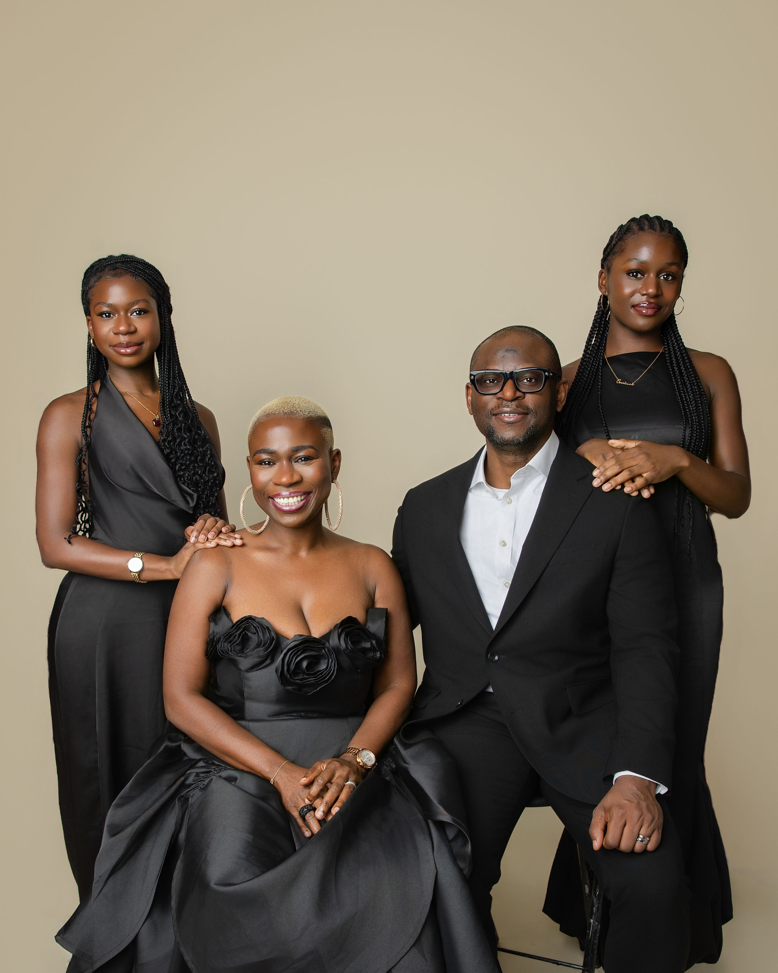 A group of people wearing black formal attire pose together for an elegant studio portrait against a neutral background.
