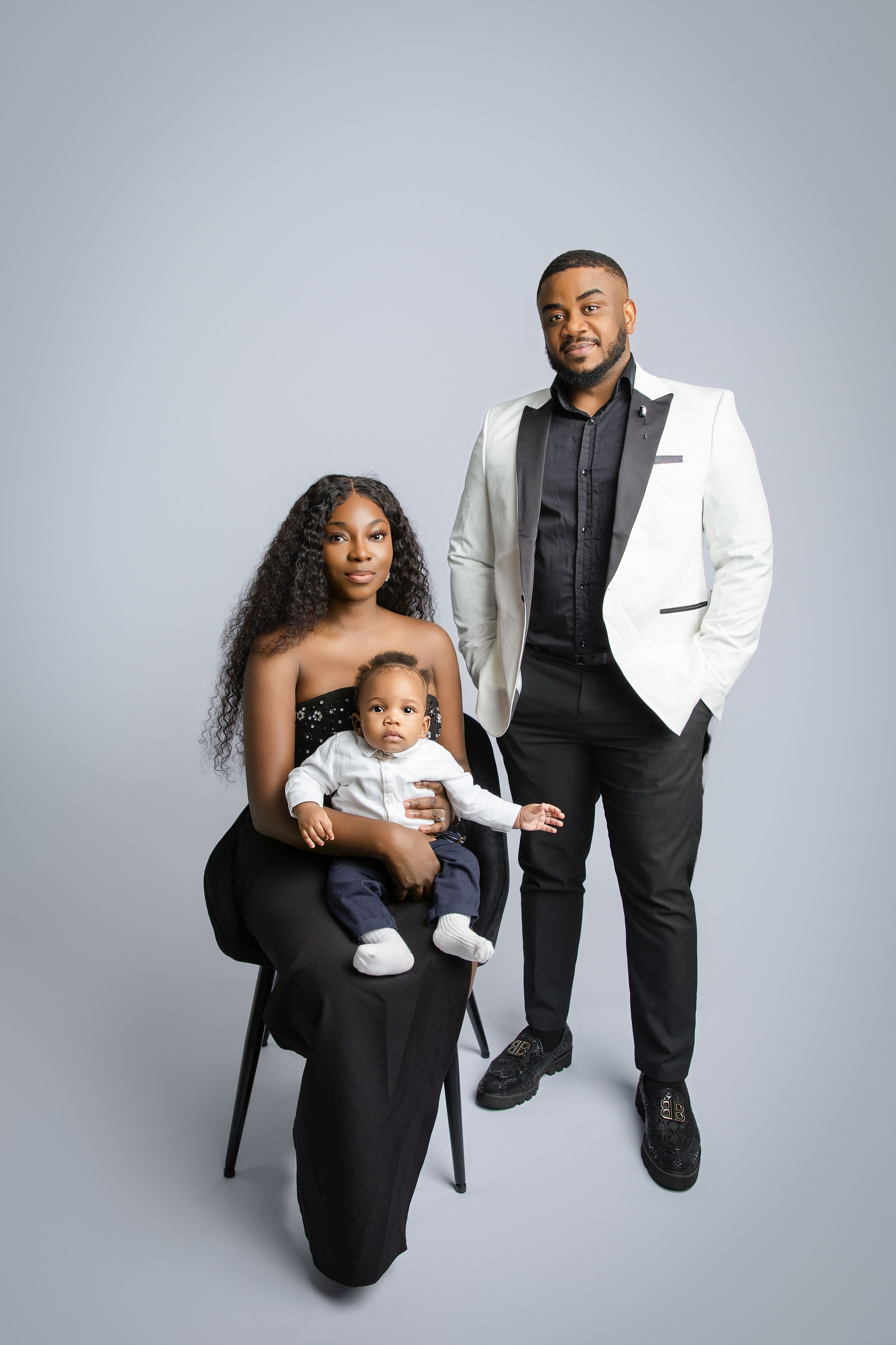 A family wearing black and white formal attire poses together against a gray studio backdrop in a series of photos.