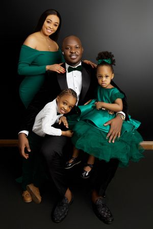 A family portrait session featuring coordinated emerald green and black formal attire against a dark background.