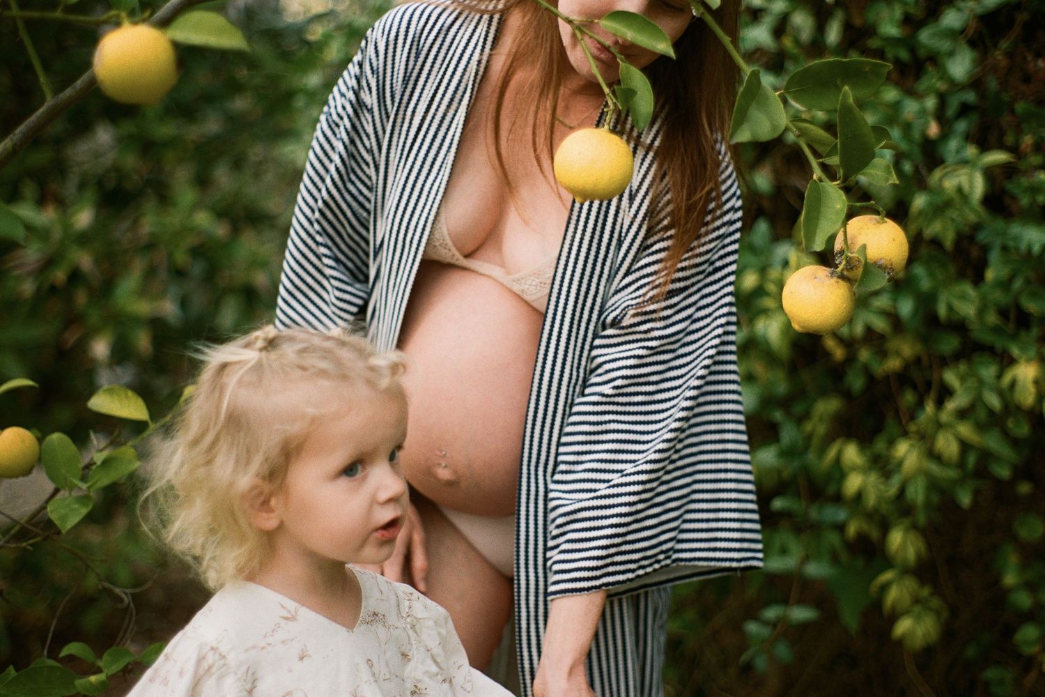 Maternity photoshoot in a citrus grove with striped robe and white dress.