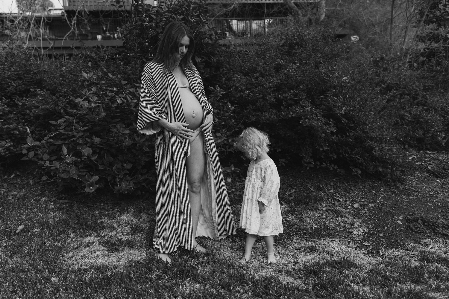 A vintage-style black and white portrait showing two figures in flowing dresses standing in a garden setting.