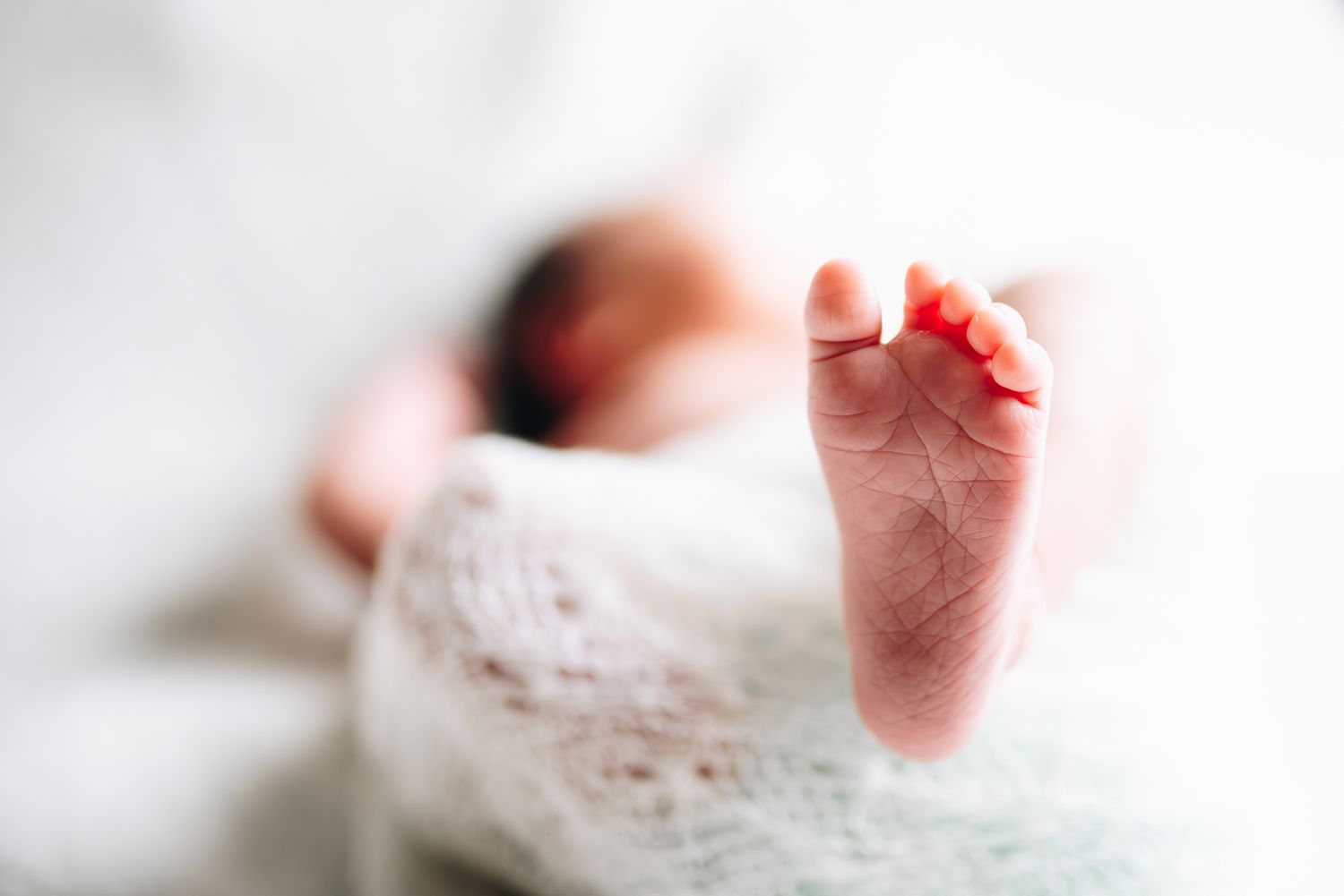Close-up photo of a tiny newborn baby foot wrapped in delicate white lace against a light background taken by Melbourne newborn photographer