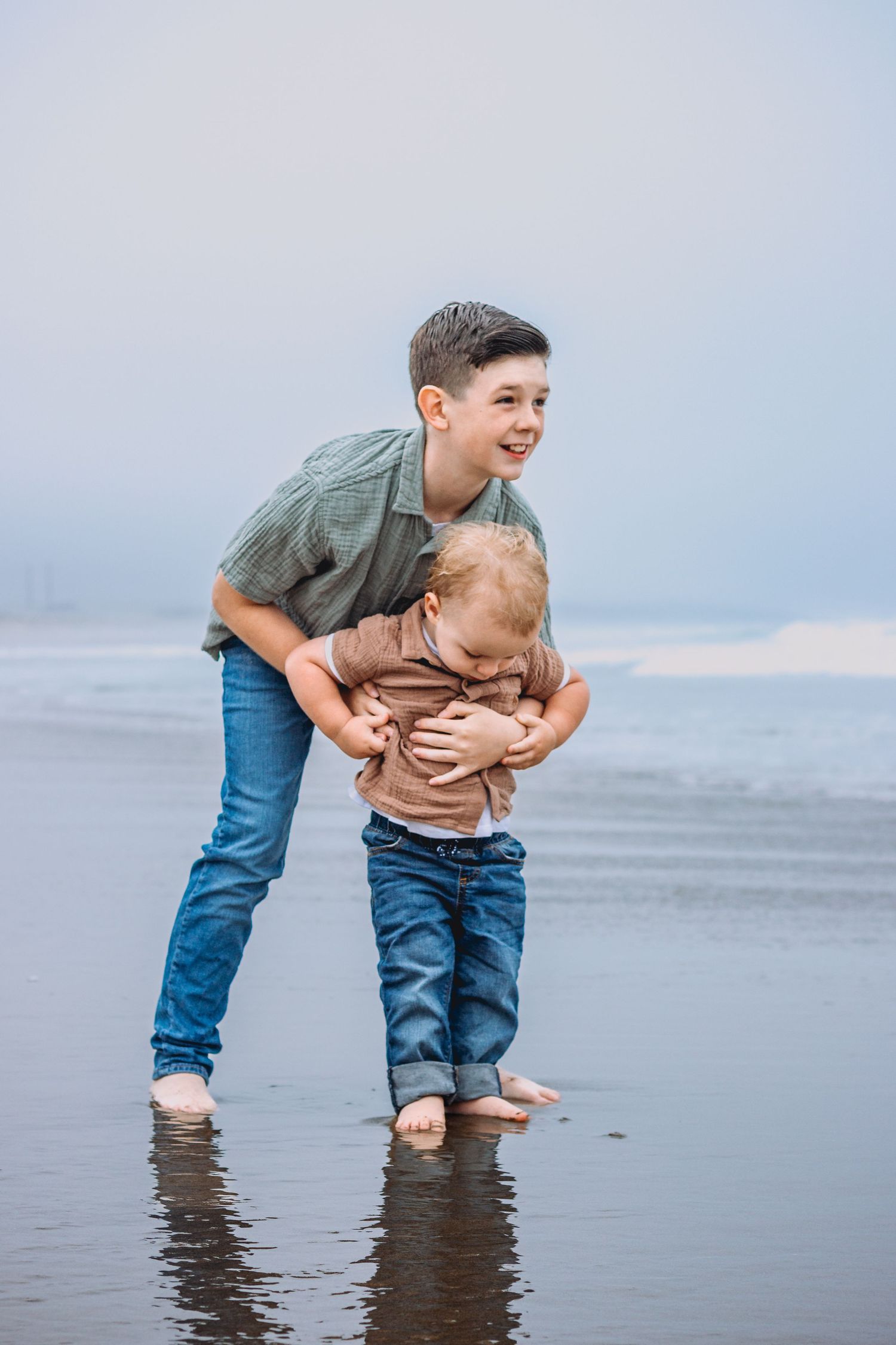 Two children play in shallow ocean water at the beach.