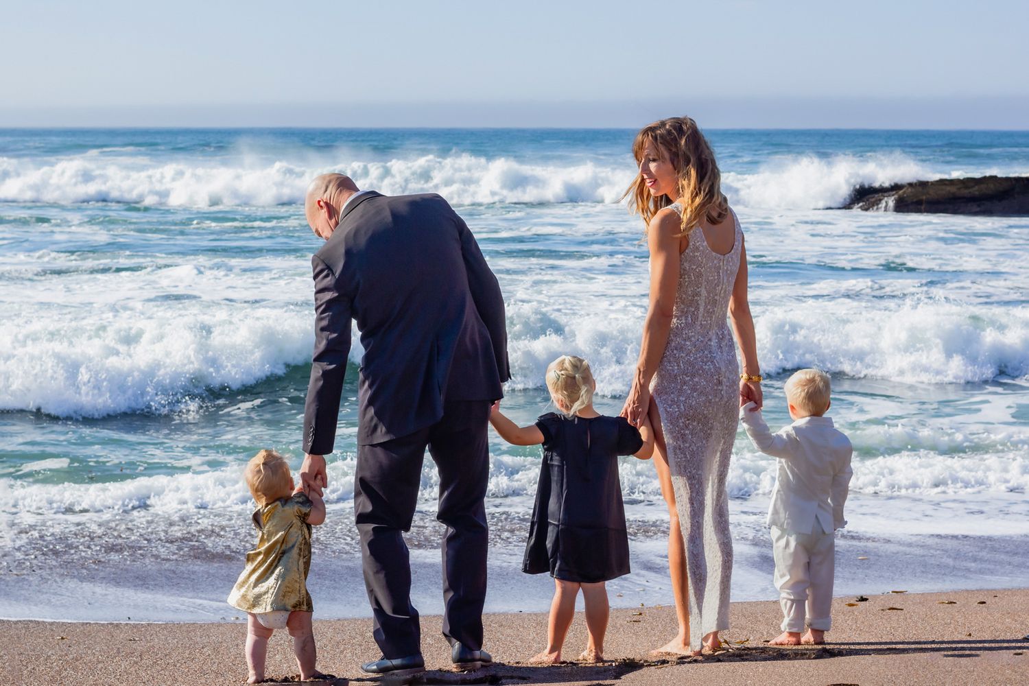 Family walking together along beach shoreline with waves crashing in background.