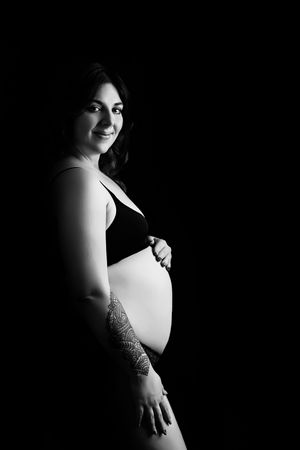 Dramatic black and white maternity portrait showing an expectant mother posing gracefully against a dark background.