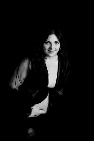 Black and white portrait photograph showing a figure in dark clothing against a dark background.
