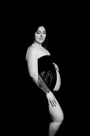 Black and white artistic maternity portrait showing an expectant mother in an intimate pose against a dark background.