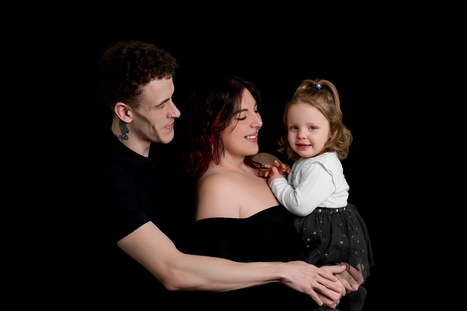 Family portrait against black background showing parents with young child in black and white outfits.
