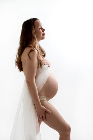 Artistic side profile maternity portrait with flowing white fabric against light background.