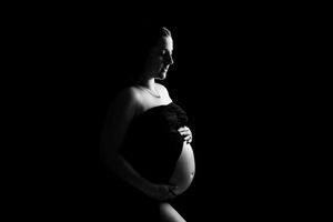 Dramatic black and white silhouette maternity photo with side lighting emphasizing the pregnant belly against dark background.