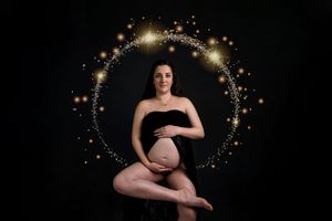 Artistic maternity photo featuring glowing golden lights in a circular halo effect against a dark background.