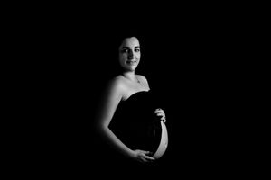 Black and white maternity photo showing silhouette of a pregnant figure against dark background.