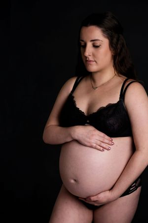 An intimate maternity portrait showing an expectant mother in black lingerie against a dark background.