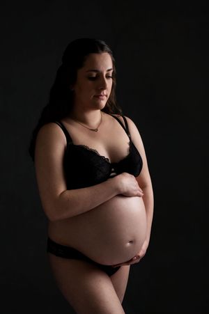 Intimate maternity portrait in dark lighting showing an expectant mother in black lingerie.