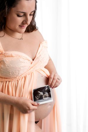 A maternity photo features someone in peach-colored attire holding an ultrasound image against their belly.