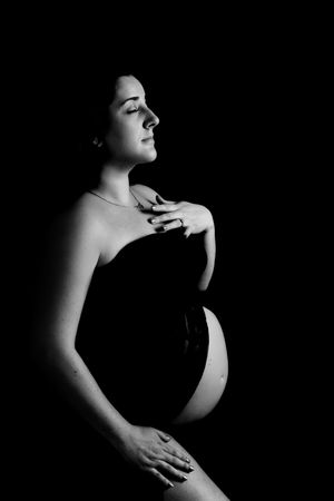 Artistic black and white portrait of an expectant mother in profile view against dark background.