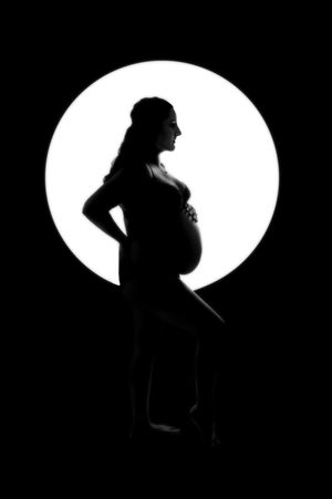 An artistic silhouette of an expectant mother against a white circular backdrop creates a dramatic contrast.