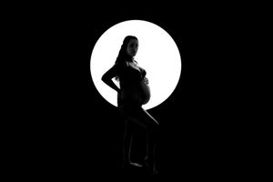 Silhouette of a pregnant figure against a bright circular light creating dramatic contrast.