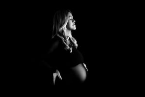 Black and white artistic maternity silhouette of an expectant mother in profile against a dark background.