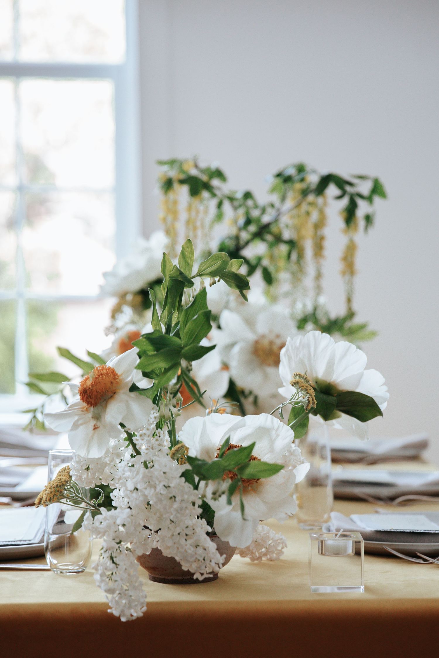 Elegant table setting with white floral centerpieces and place settings in a bright, airy dining room.