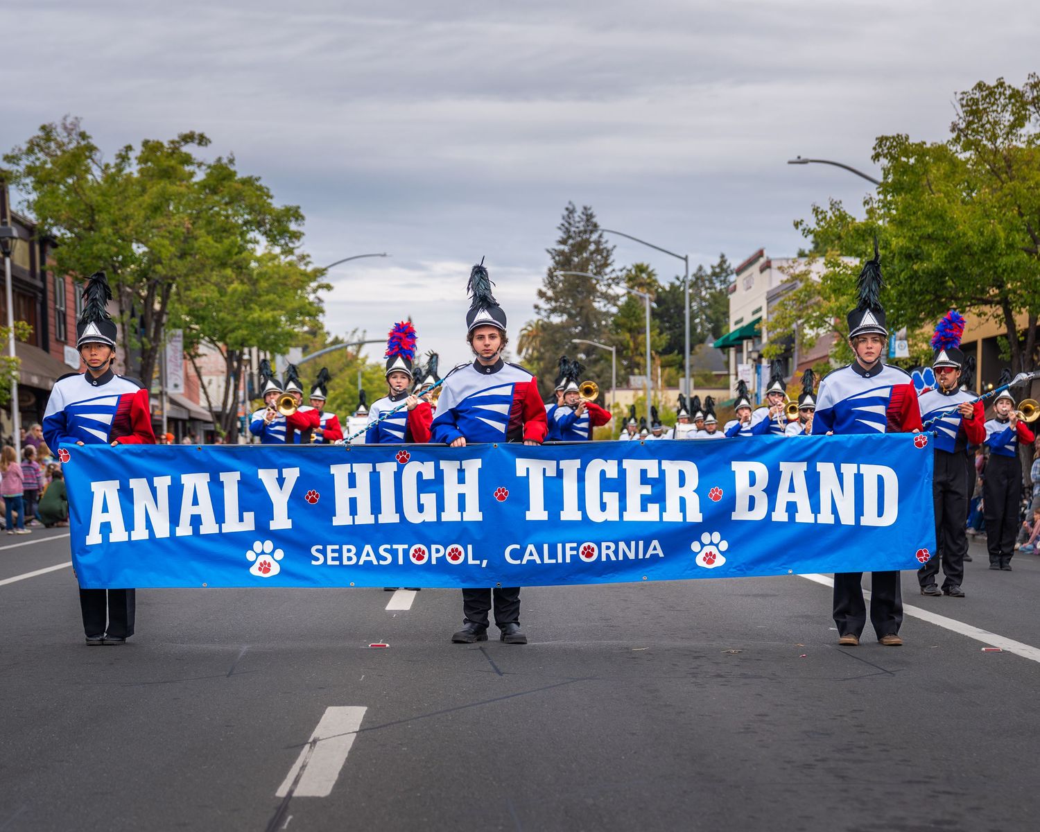 High school marching band members carry a blue banner in a parade through downtown Sebastopol, California.