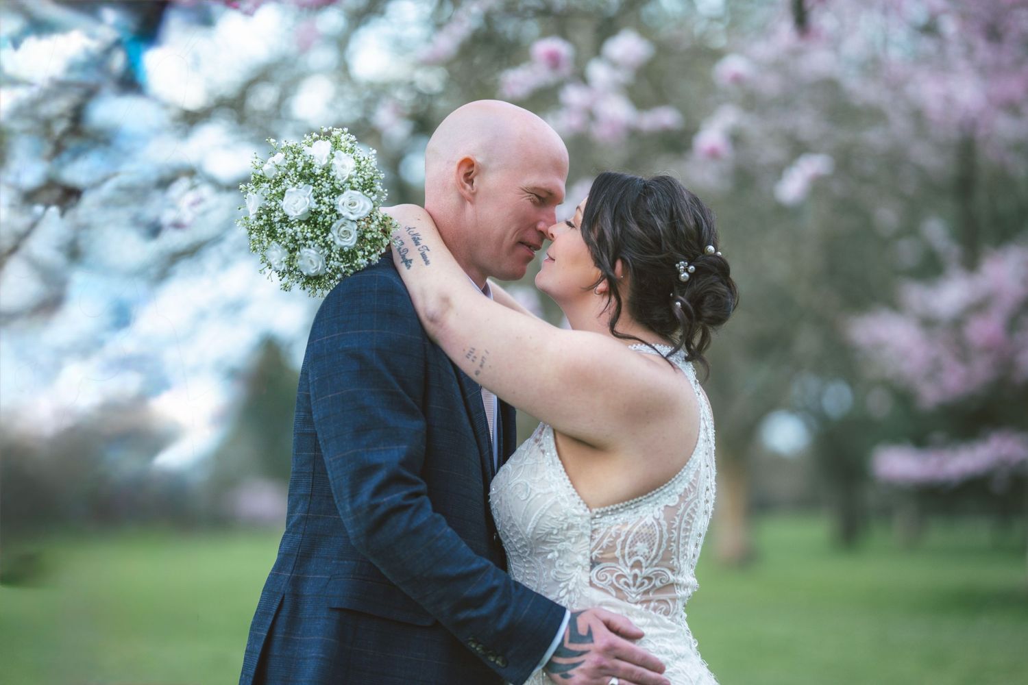 A couple embraces under blooming cherry blossom trees in a spring garden setting.