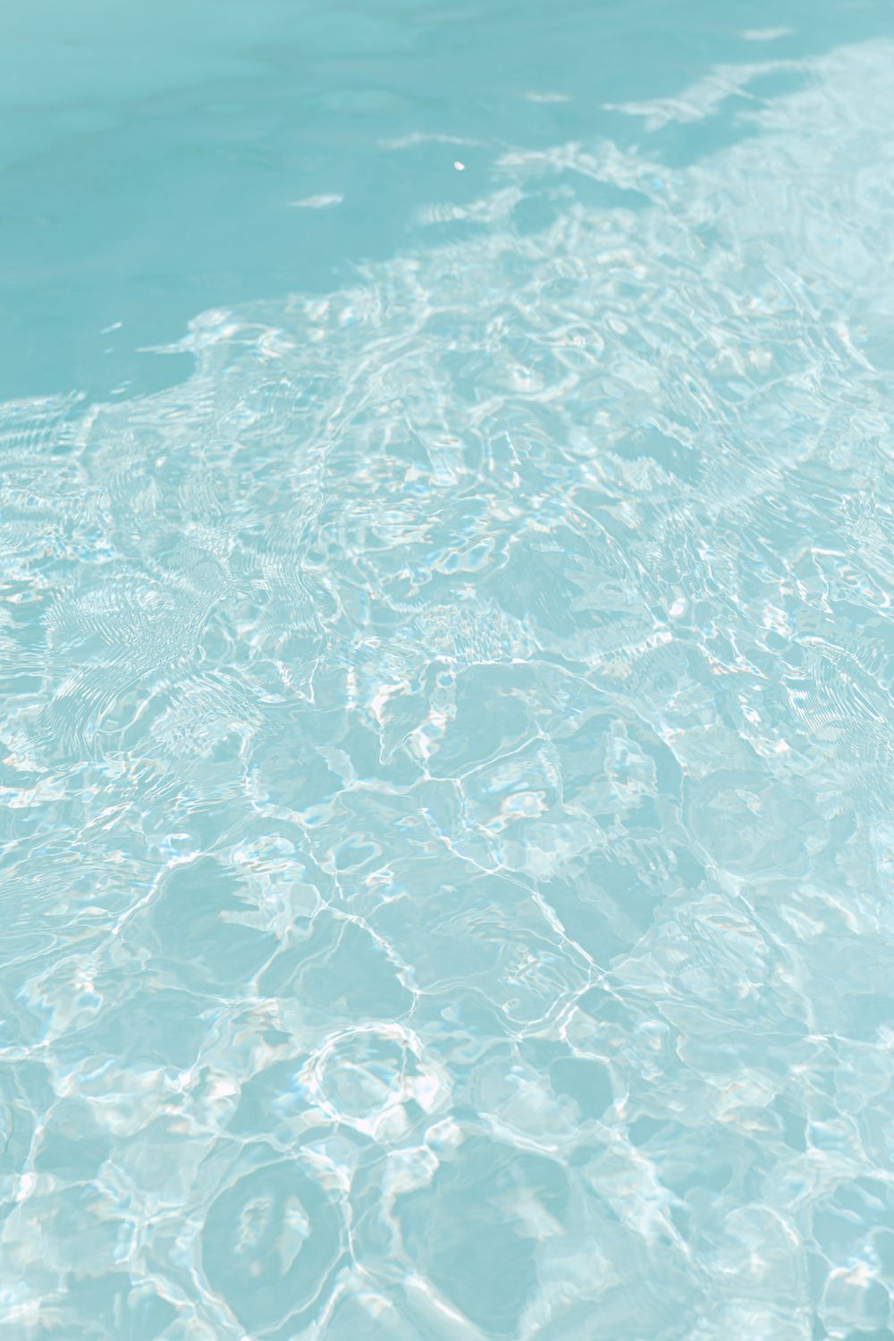 Crystal clear turquoise water ripples in bright sunlight creating abstract patterns.