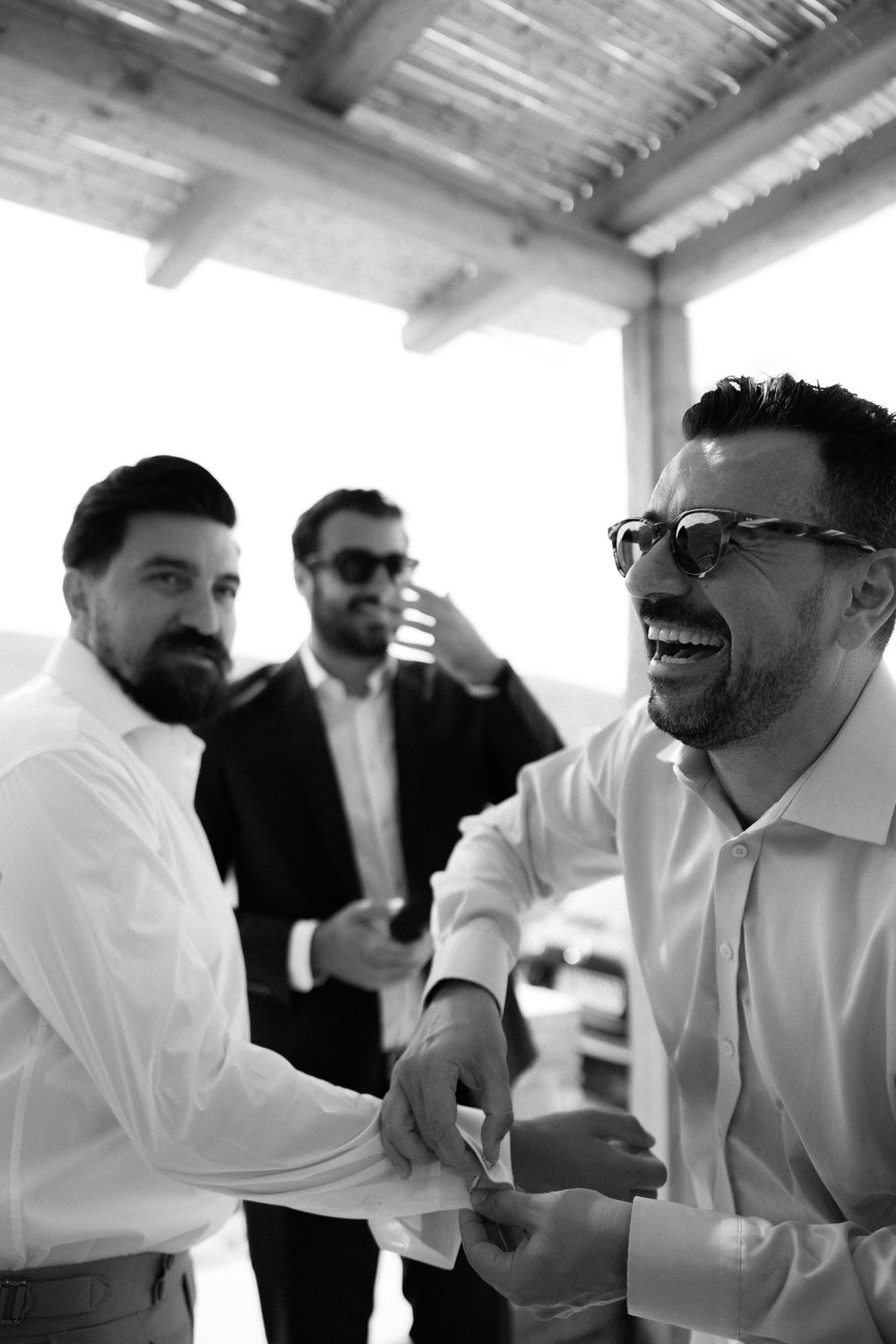 A candid black and white photo of friends sharing a joyful moment at a gathering. Destination wedding photographer Kythnos