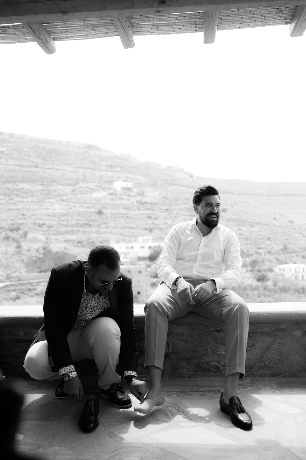 Two people sharing a relaxed moment on a terrace overlooking rolling hills. Destination wedding photographer Kythnos