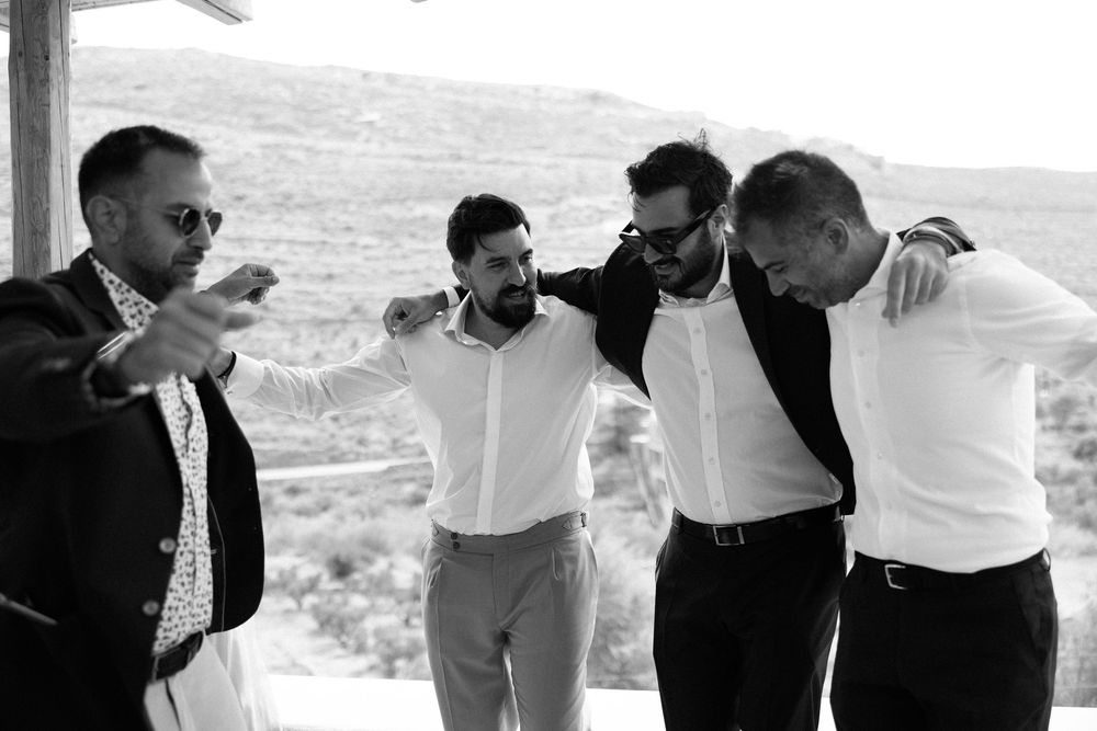 Group of friends in formal attire sharing a celebratory moment on a covered patio. Destination wedding photographer Kythnos