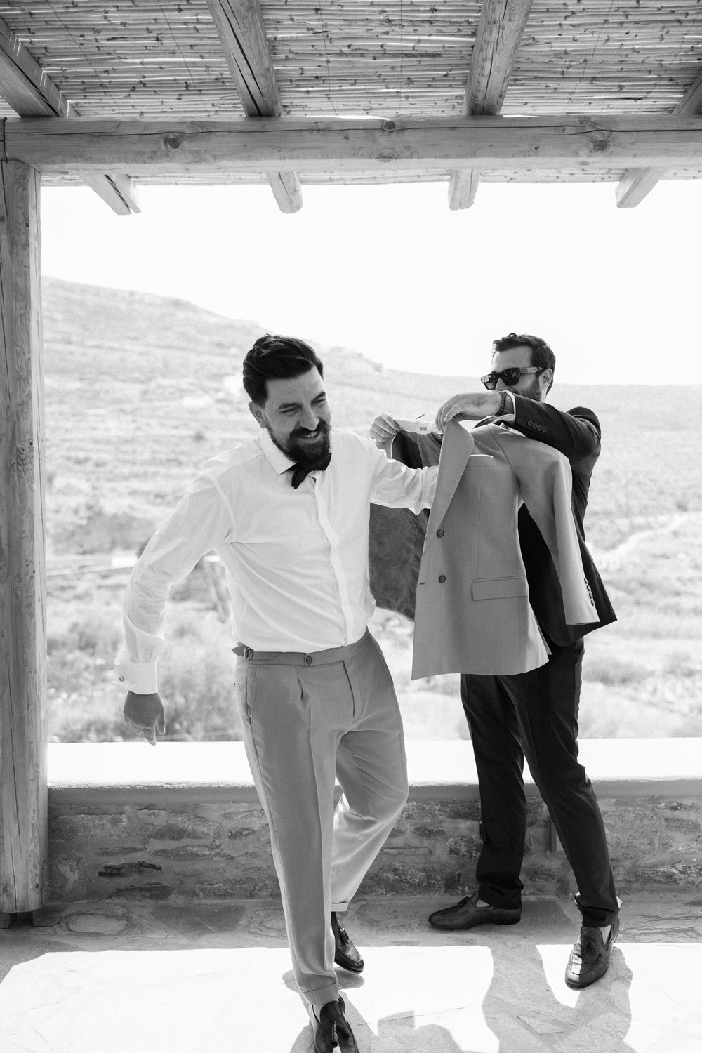 Candid moment of people getting ready in formal attire on a covered terrace. Destination wedding photographer Kythnos