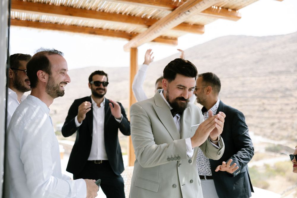 Wedding party celebrates under covered patio in desert setting. Destination wedding photographer Kythnos