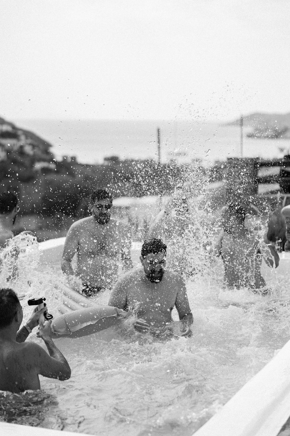 Group of people splashing and playing in pool captured in black and white photography.