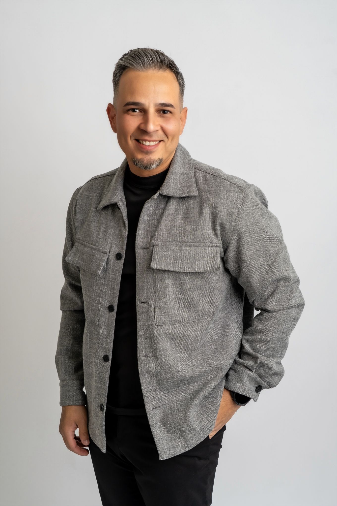 Professional studio shot of person in gray utility jacket smiling against white backdrop.