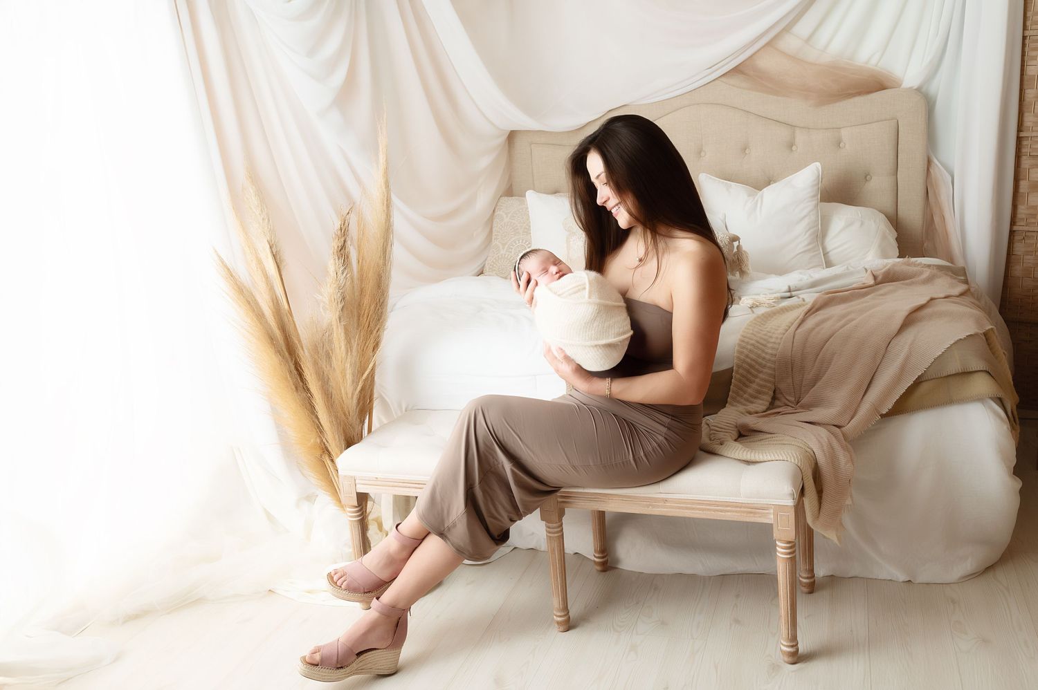 Tender moment between parent and infant in bright minimalist setting with draping fabric and natural light.