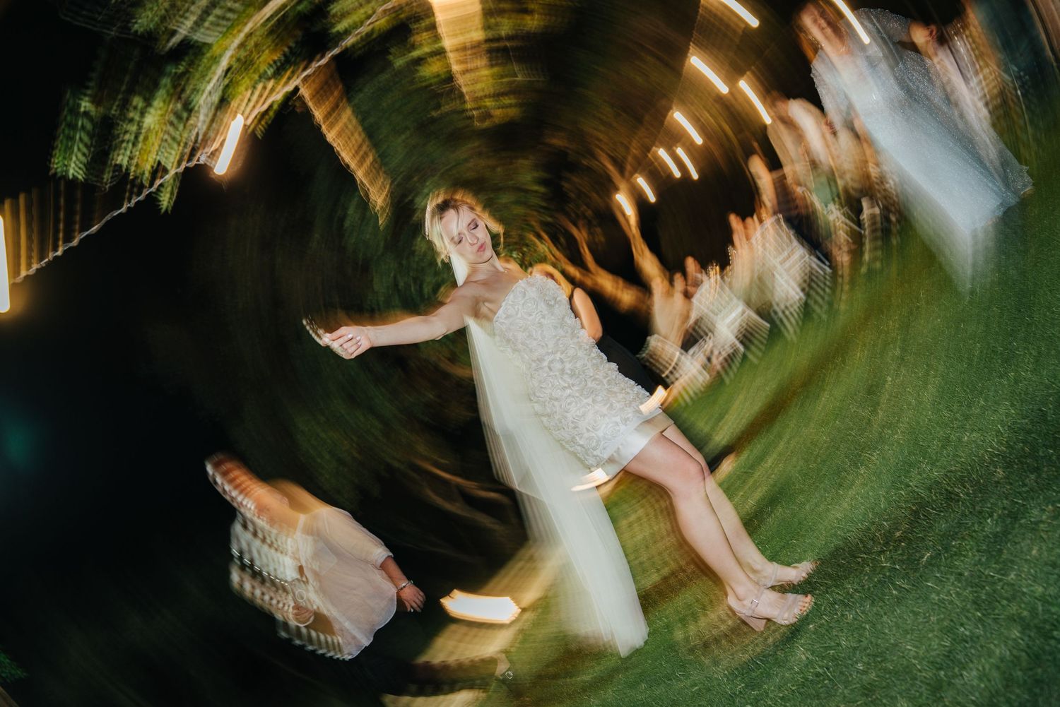 A group of people dancing in a circular motion on a green dance floor at a celebration event.