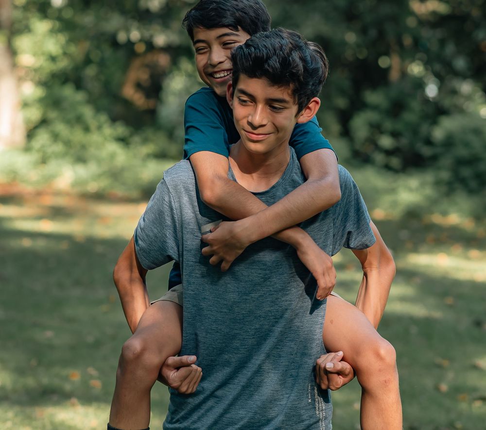 Two people sharing a piggyback ride while smiling and laughing in a sunny outdoor setting.
