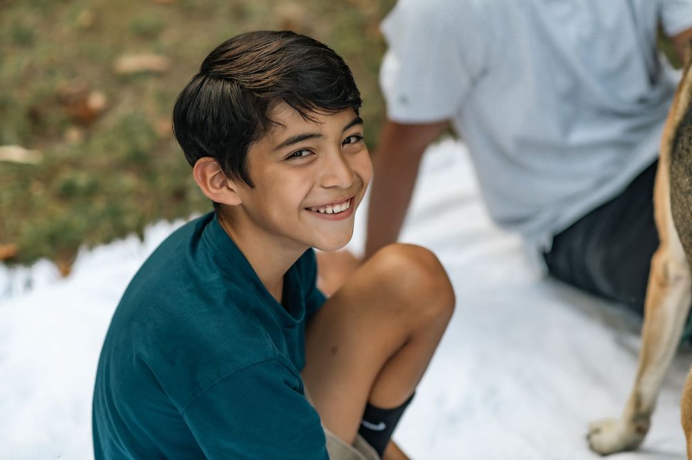 Young person smiling brightly while sitting outdoors on a sunny day.