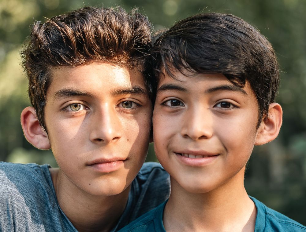 Two young brothers share a close moment together outdoors with natural bokeh background.