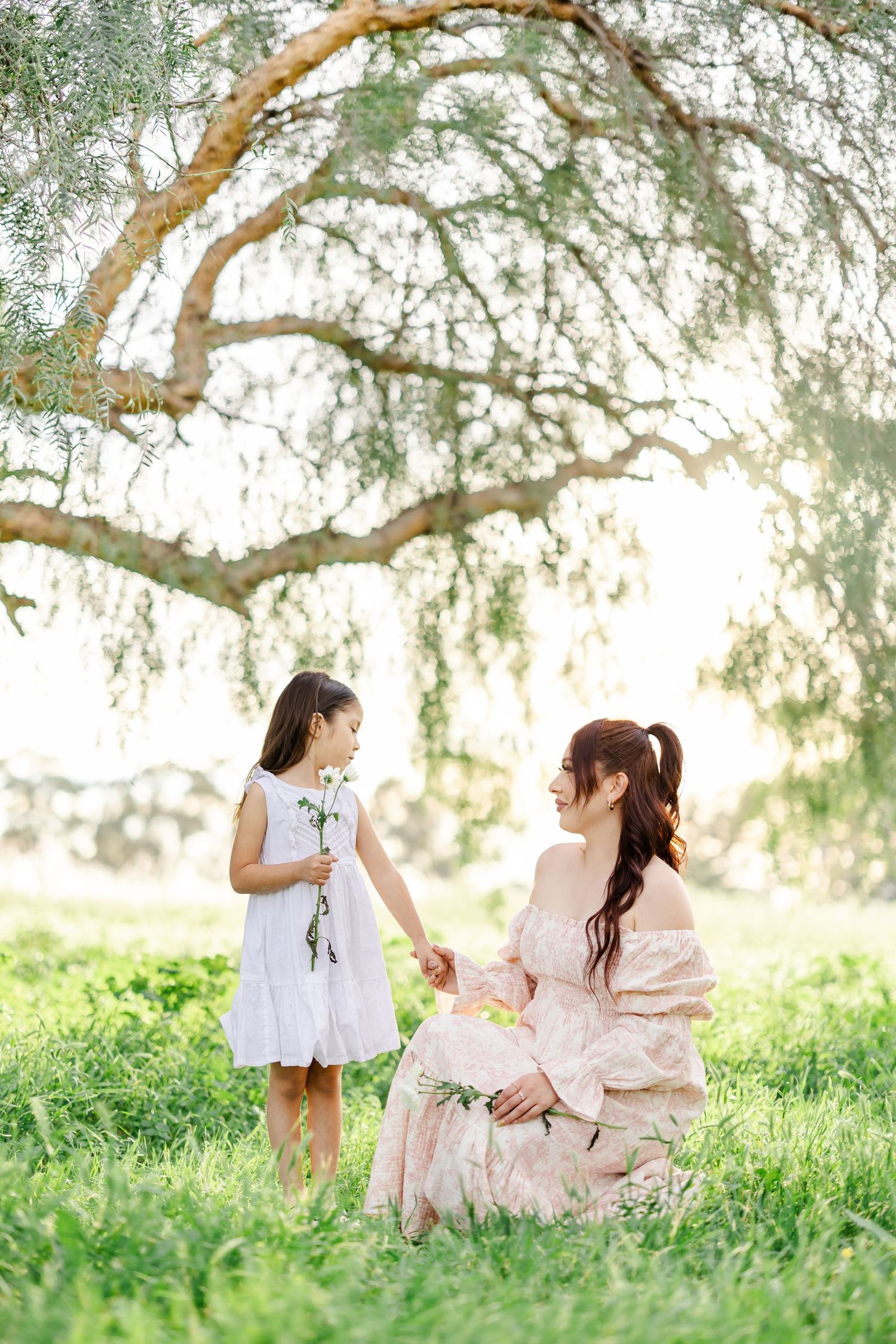 Whimsical outdoor photoshoot under a sprawling tree with flowing dresses in soft natural light.