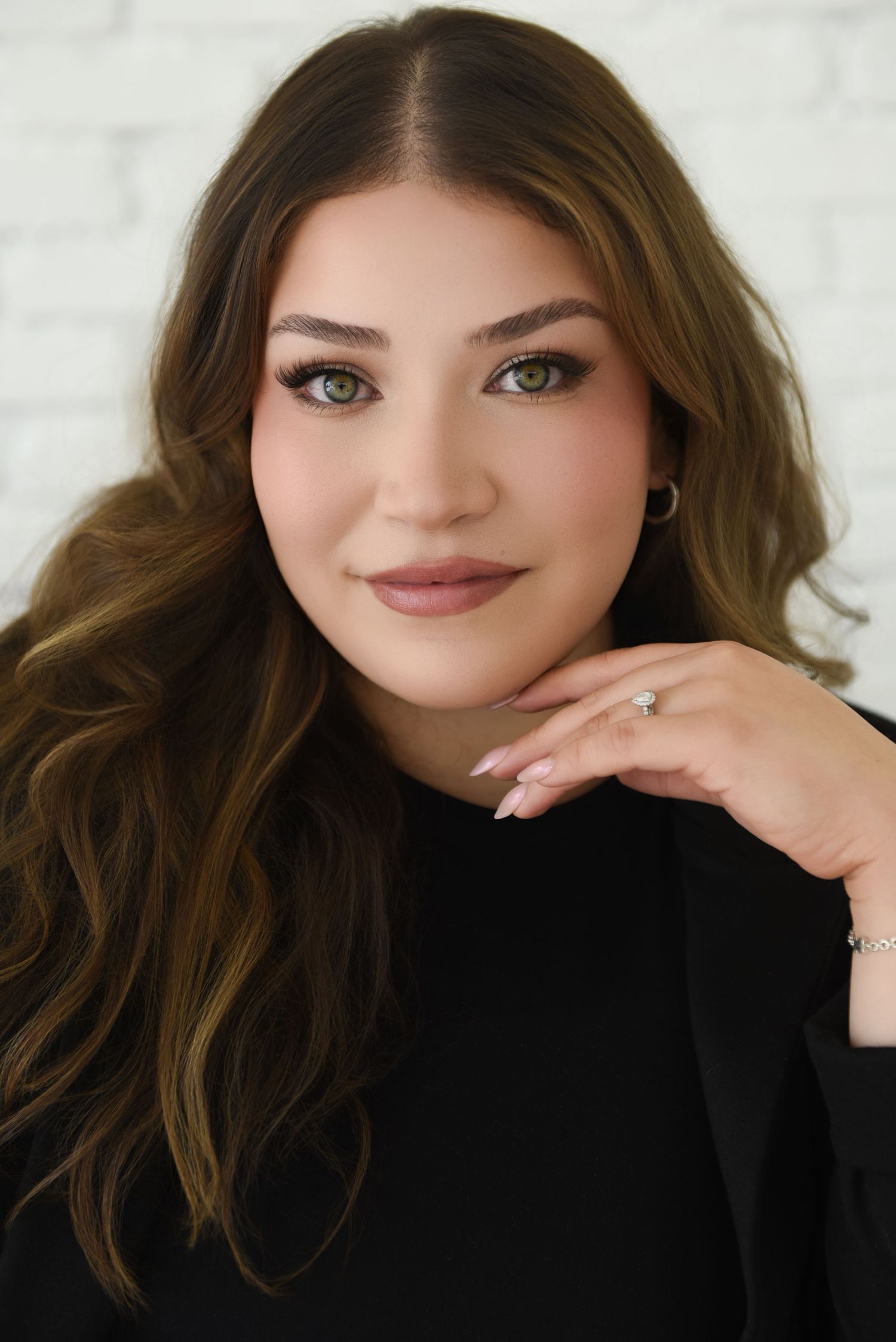 Professional headshot portrait with wavy brown hair and black top against light background in multiple poses.