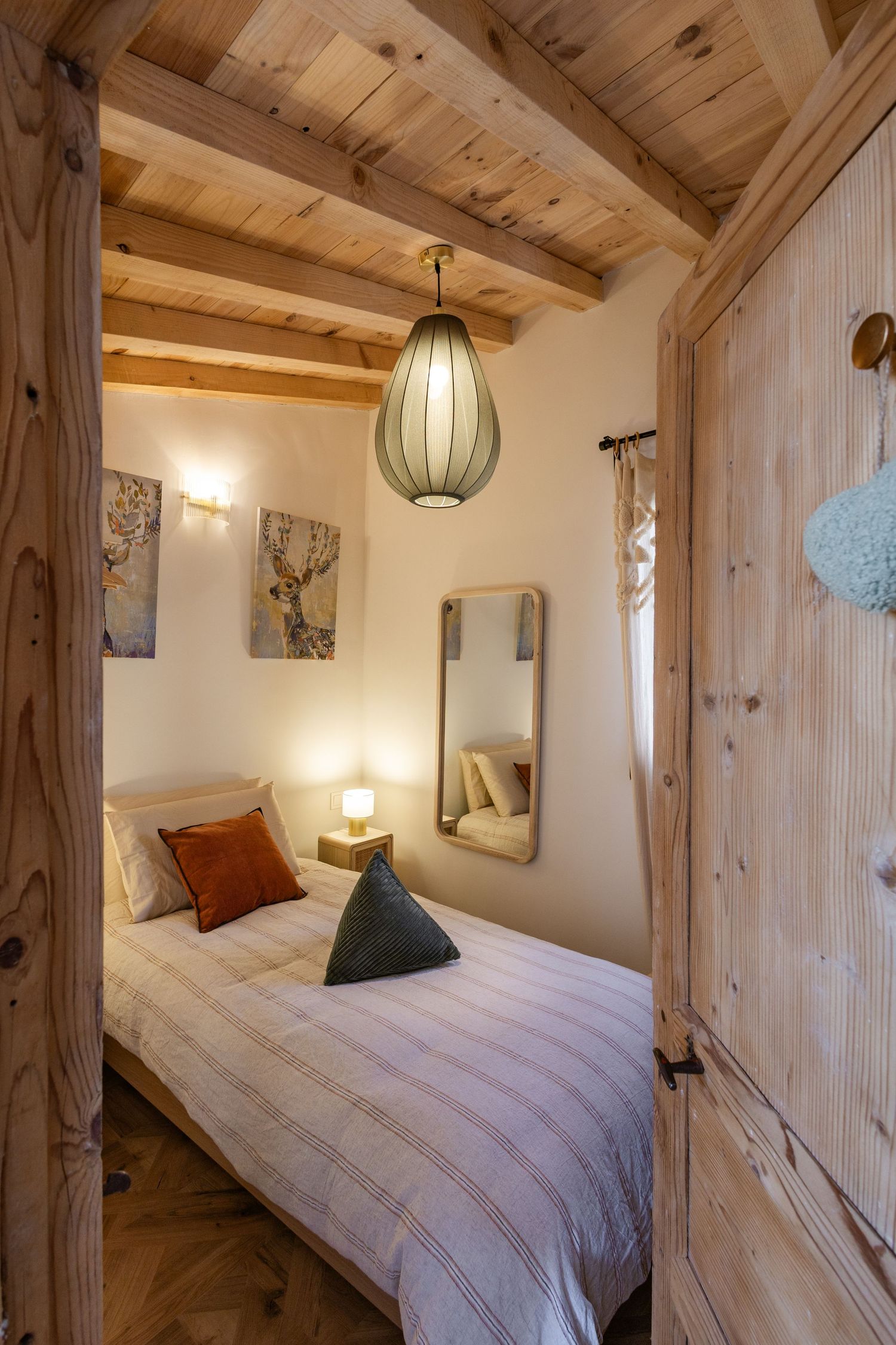 Cozy rustic bedroom with wooden beams, pendant light, and striped bedding in warm neutral tones.