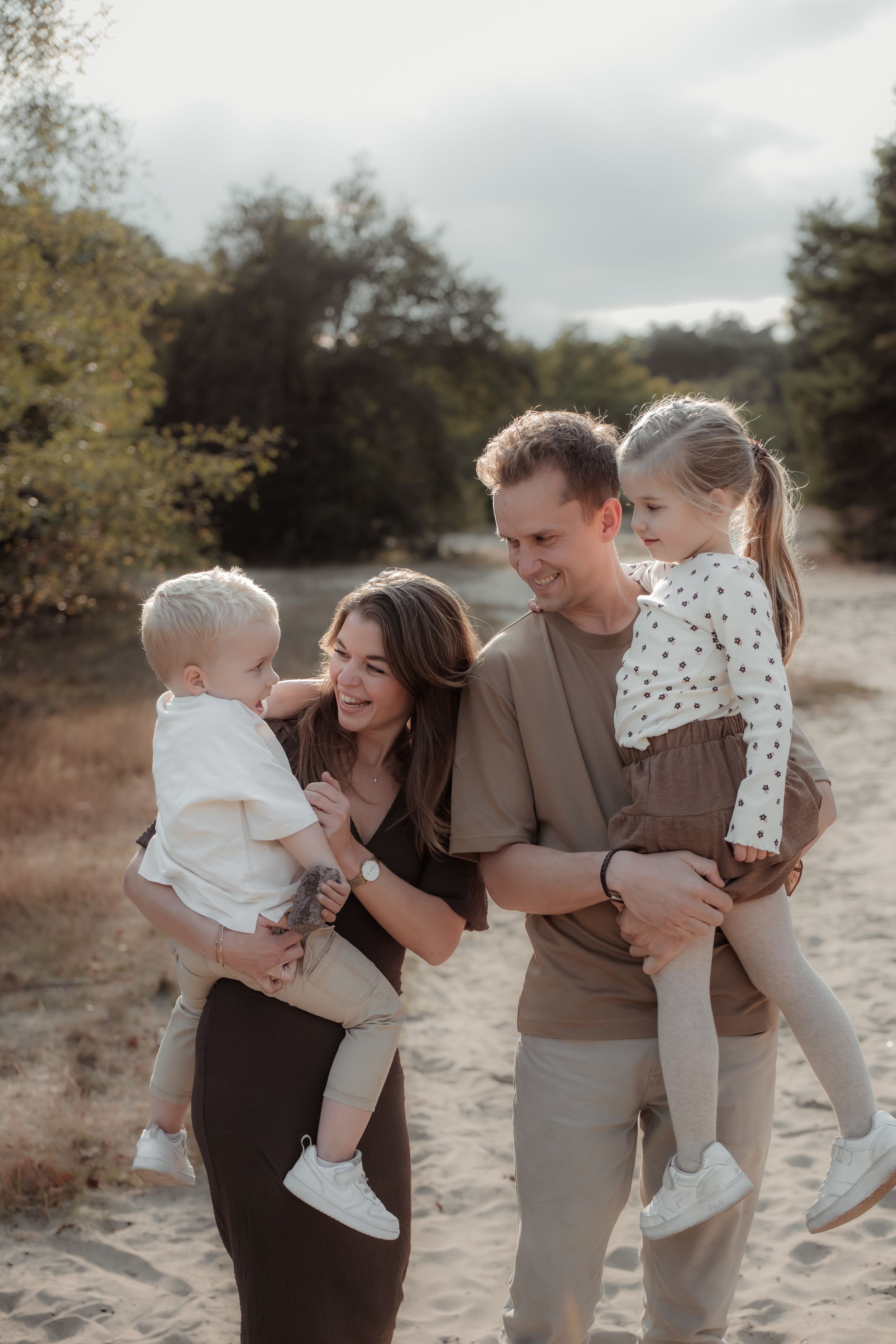 A family wearing neutral tones shares joyful moments together on a sandy path surrounded by autumn foliage.