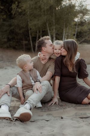 A family shares tender moments while sitting together on a sandy beach during a photo session.