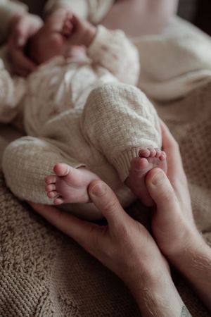A tender close-up of tiny newborn baby feet being gently held by adult hands against a textured beige blanket.