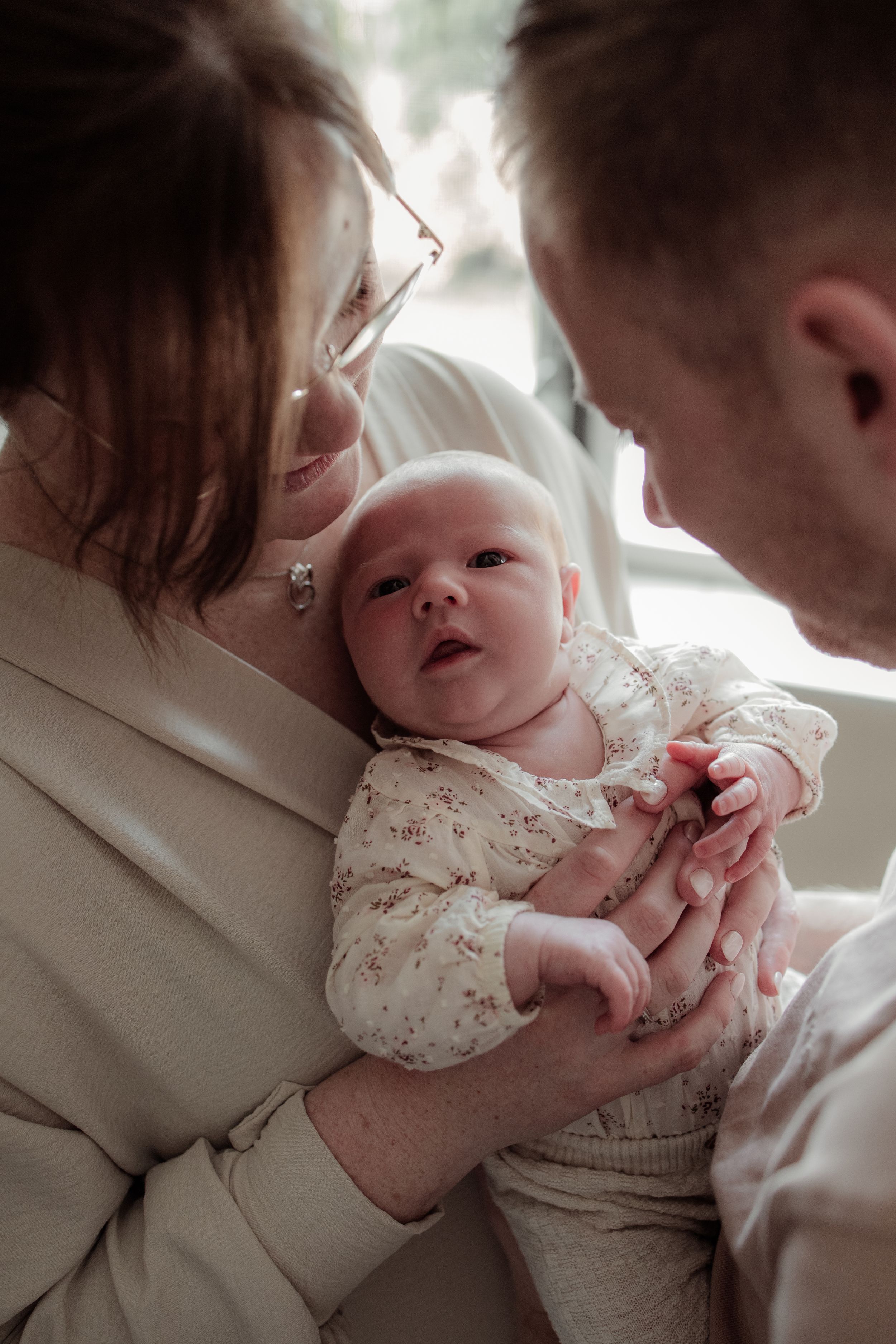A tender moment captured in soft light shows a baby in a delicate white dress being cradled gently.